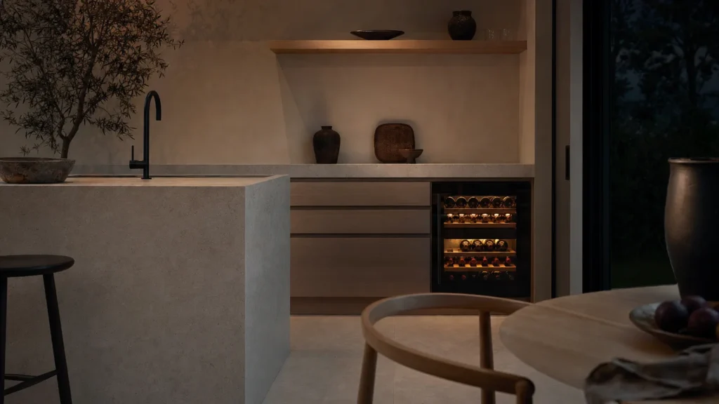 Cuisine calme le soir, seule la lumière intérieure d’une cave à vin sous plan éclaire la pièce