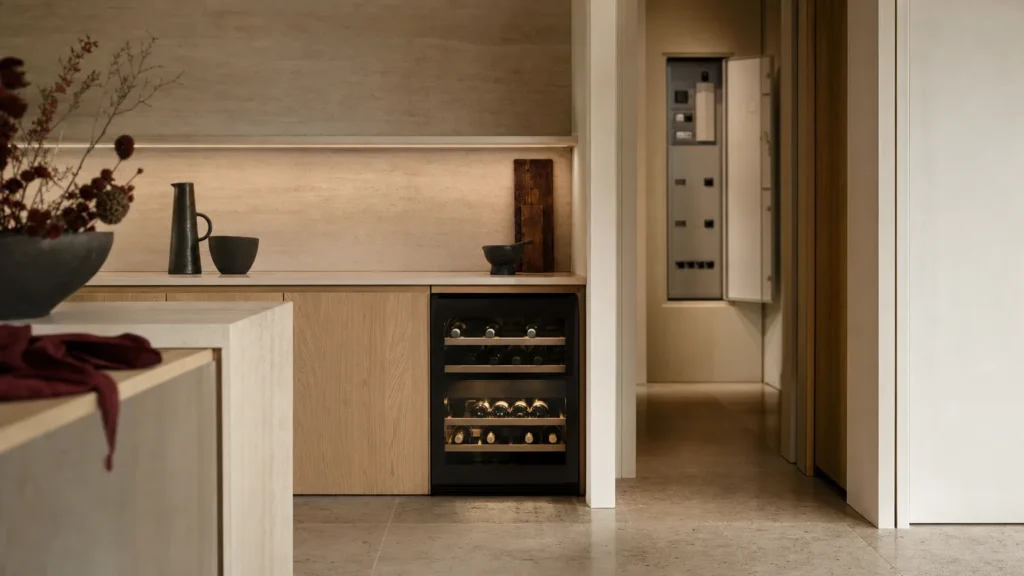 Cuisine sobre au crépuscule, cave à vin sous plan éclairée et, au fond du couloir, un tableau électrique entrouvert